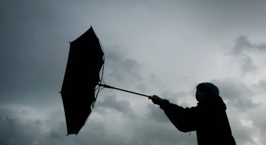 Silhouette einer Person mit einem aufgewehten Regenschirm vor dramatischem Himmel. Der **Orkan** kämpft gegen den Schirm.