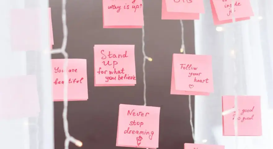 Rosa Haftnotizen mit inspirierenden Affirmationen wie "Think BIG" und "Never stop dreaming" hängen an einer Lichterkette.