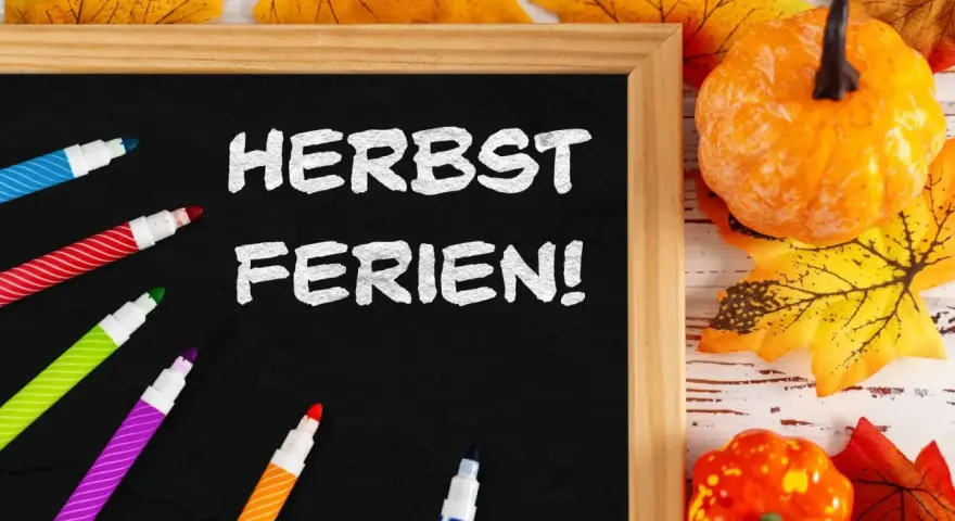 Bunte Stifte und Herbstdeko umrahmen eine Tafel mit der Aufschrift "Herbstferien!". Zeit für die Herbstferien Baden-Württemberg 2025!