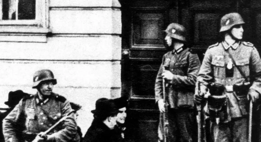 Soldaten der Gestapo stehen Wache. Ein Mann mit Gewehr im Vordergrund, zwei weitere im Hintergrund.