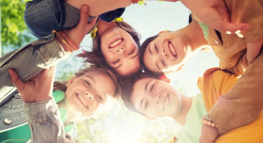 Vier lachende Freunde bilden einen Kreis, ihre Gesichter von unten nach oben aufgenommen. Perfekt für die Ferien in Hessen!
