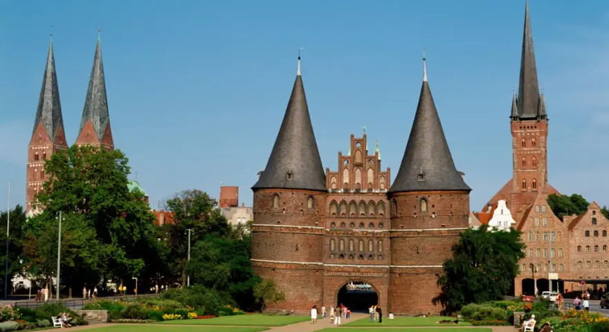 Holstentor in Lübeck, ein Wahrzeichen für Ihre **Ferien Schleswig-Holstein 2025**. Historische Backsteinarchitektur mit Türmen und grünen Parks.