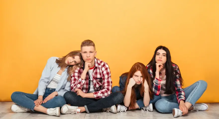 Vier junge Leute sitzen auf dem Boden, die Gesichter zeigen deutliche Langeweile.