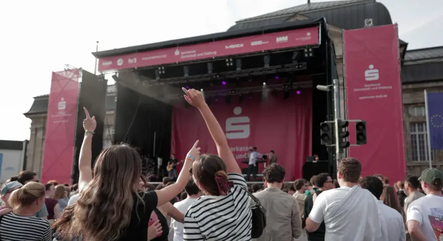 Menschen jubeln bei einem Open-Air-Konzert vor einer Bühne mit Sparkassen-Logo.