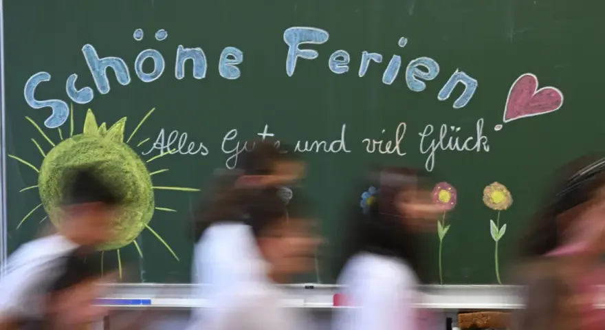 Kreidetafel mit "Schöne Ferien" und einem lachenden Smiley, bereit für die herbstferien 2025 nrw. Kinder huschen vorbei.