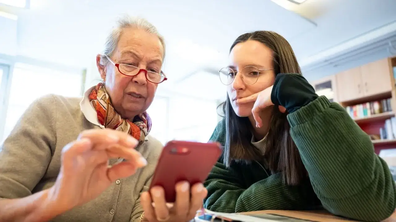 Eine ältere Frau zeigt einer jungen Frau, die zur genz gehört, etwas auf ihrem Handy.
