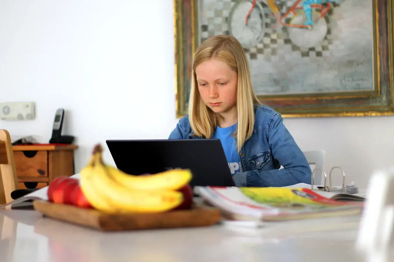 Ein Mädchen lernt konzentriert am Laptop, gestärkt durch ihre Selbstwirksamkeit. Obst liegt bereit für eine gesunde Pause.