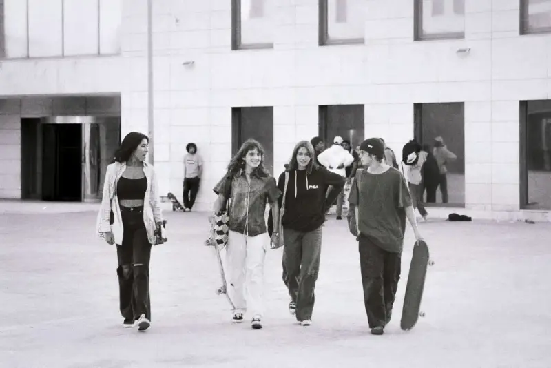 Vier junge Leute, die zur genz gehören, gehen mit Skateboards vor einem modernen Gebäude.